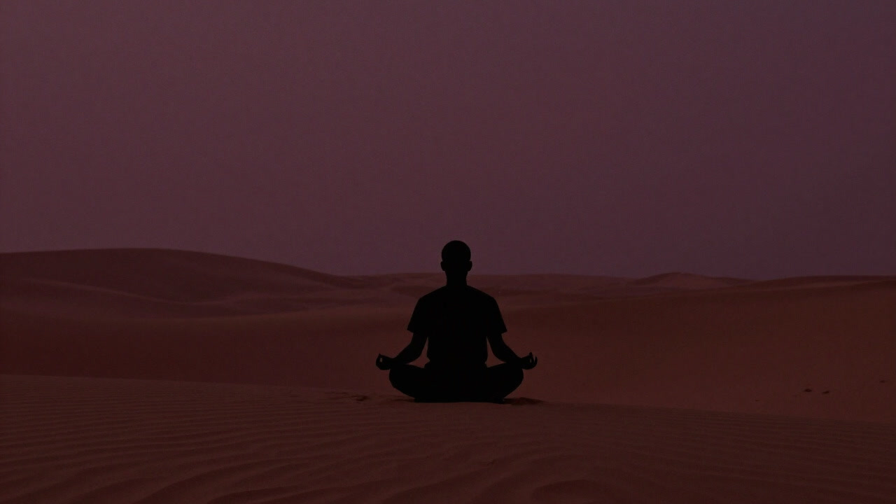 広大な砂漠の中で、何も持たずに瞑想する人物のシルエット