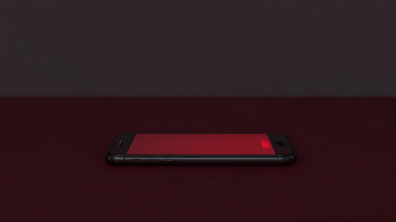 暗い机の上でほのかに赤く光るバッテリー残量警告のスマホ画面