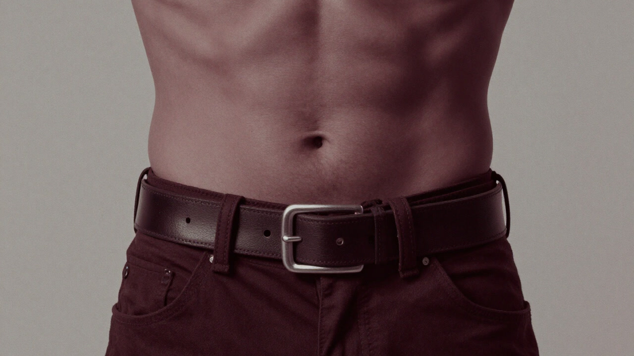 無数のベルト穴に囲まれ、苦痛の表情を浮かべる腰回りのクローズアップ画像