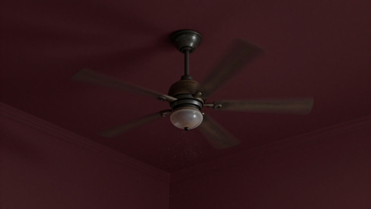 Close-up of a ceiling fan spinning silently with dust particles drifting in the air.