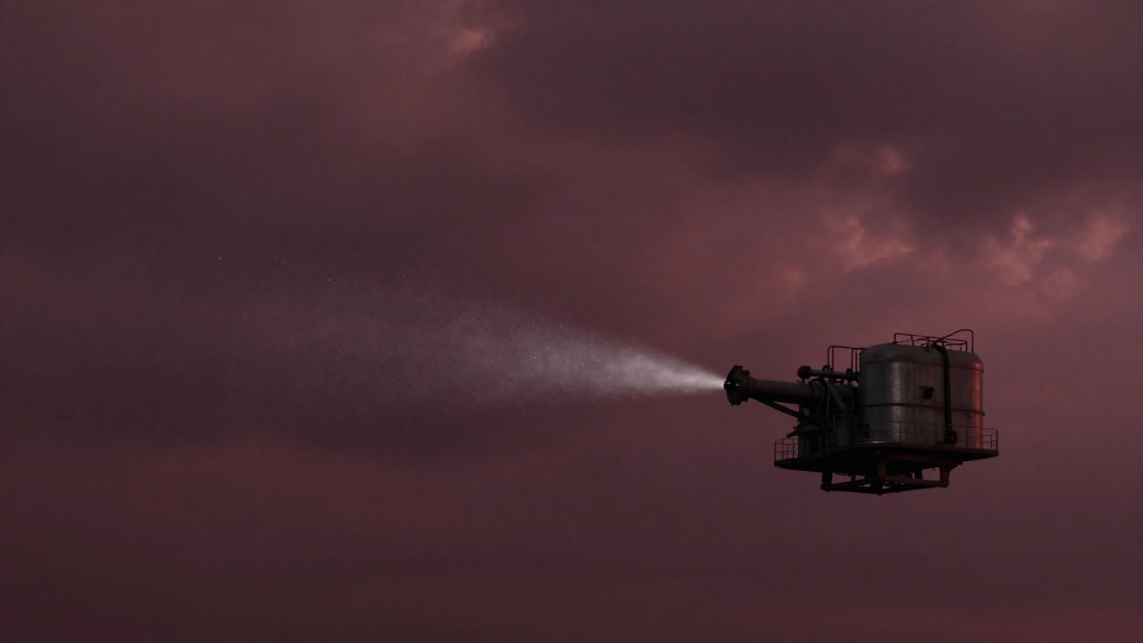 厚い雲の中で装置から白い粒子が噴き出し、遠くに地平線がかすんで見える風景