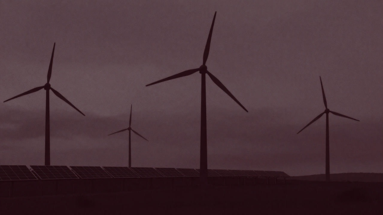Eerie scene of giant wind turbines and solar panels silhouetted against an overcast sky