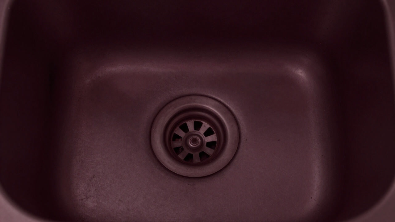 A photograph of a drain half-buried in pipes and debris, asserting its presence under the sink.