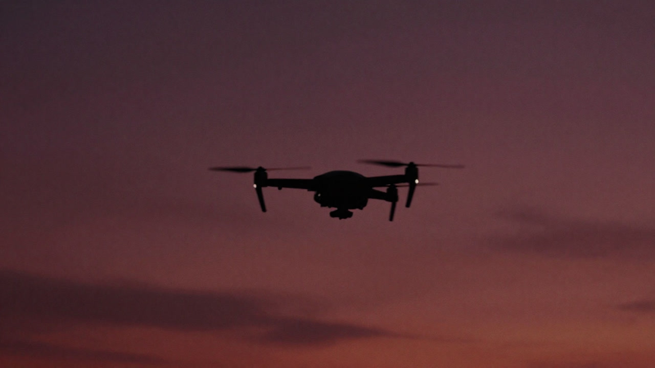 Silhouette of a small unmanned aerial vehicle flying against a wide sky background, its propellers spinning instead of wings.