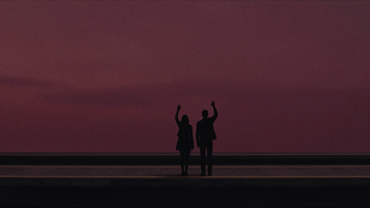 Silhouette of two figures waving at each other on a station platform at sunset