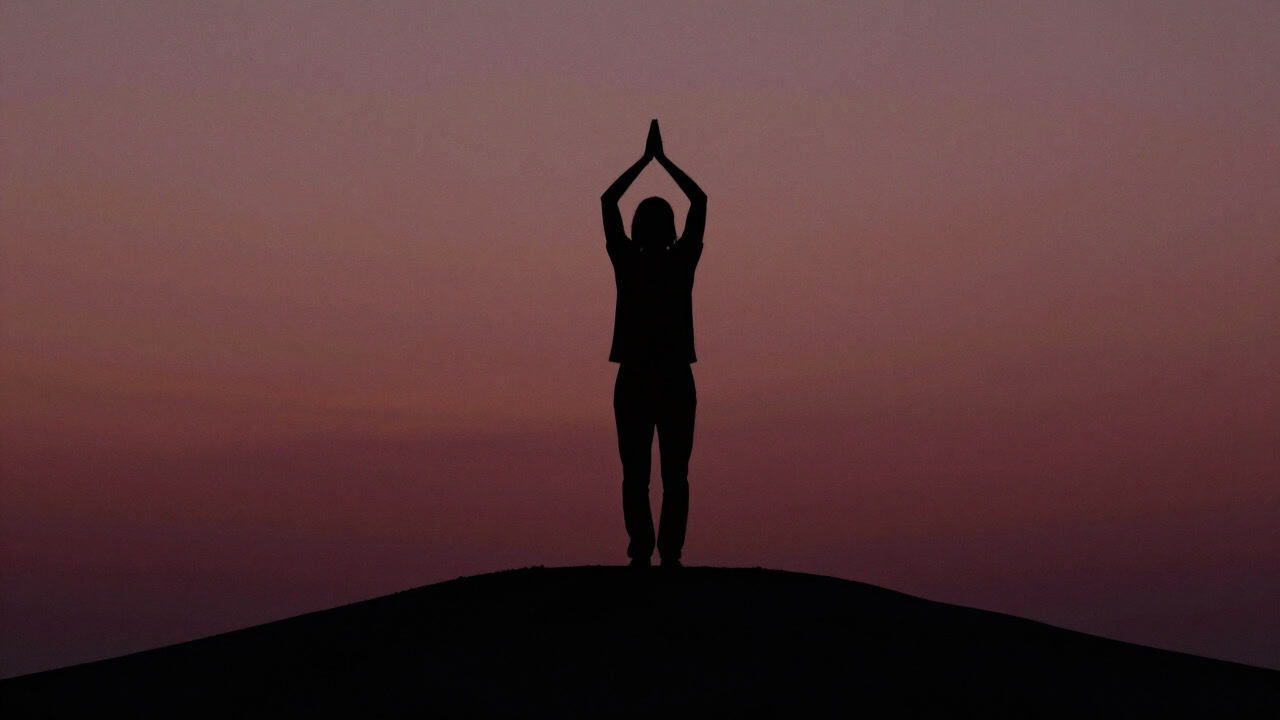 Silhouette of a figure on a hilltop raising both hands in supplicatory prayer toward the void