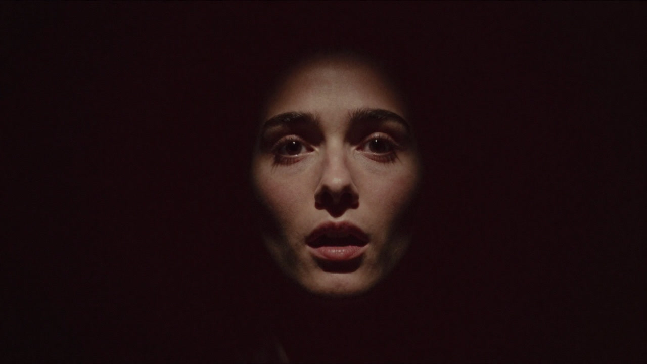 An image in darkness showing a human face illuminated momentarily, revealing a fleeting emotional expression.