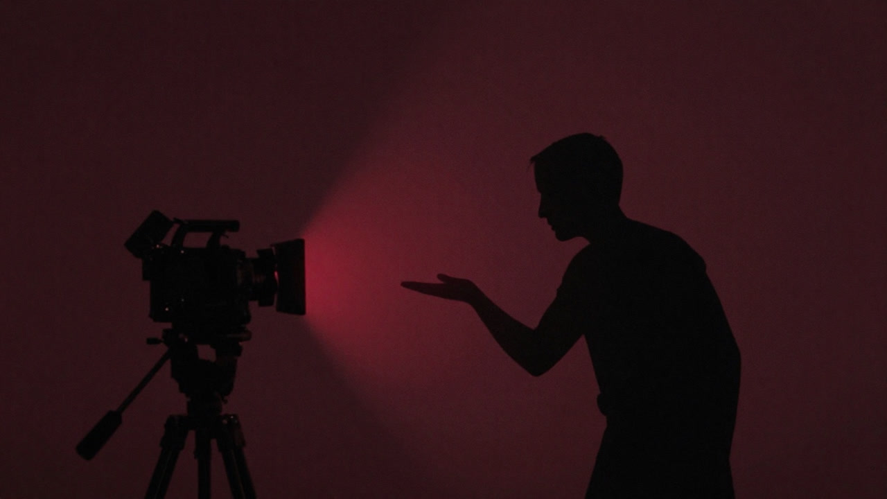 Silhouette of a person nervously delivering a lecture to a mic under the glow of a red recording light