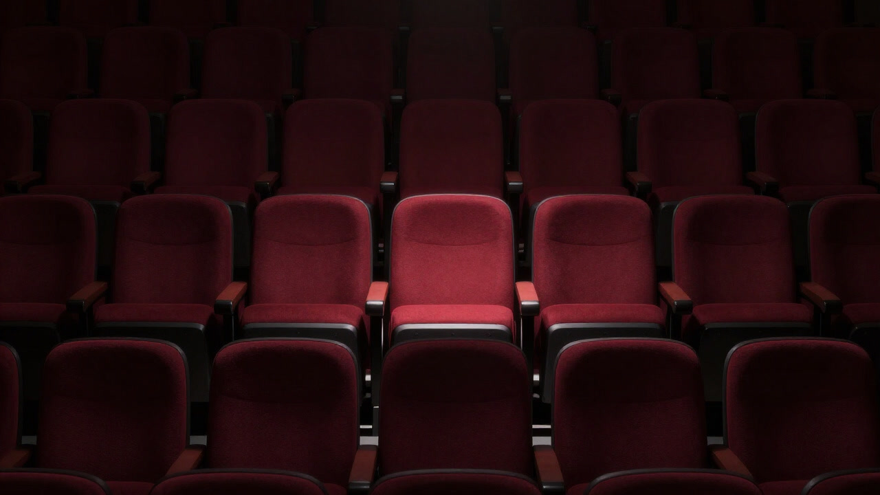 An image capturing a single red empty seat in a fully occupied theater, drawing the gaze of the audience.
