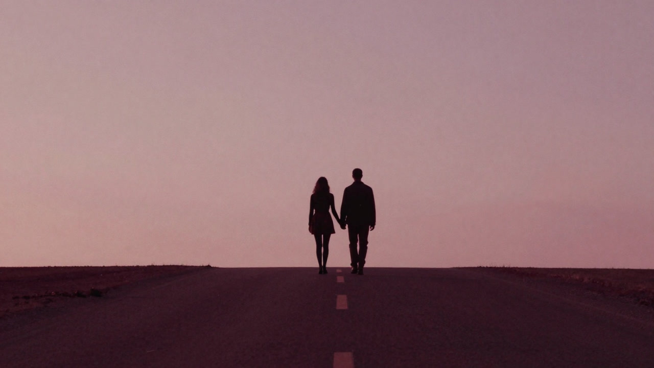 Silhouette of a couple walking in lockstep along a flat road that stretches endlessly.