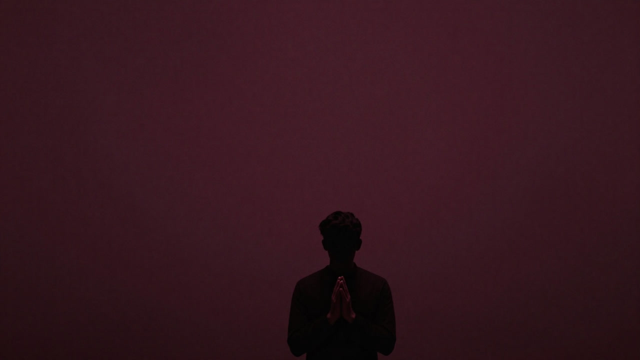 Silhouette of a person clasping hands and staring into the void