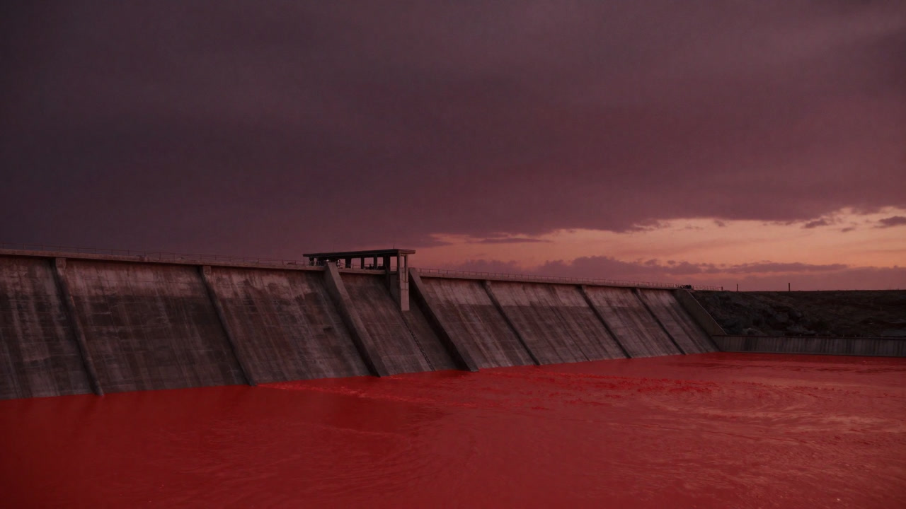 Photo of a colossal earthen embankment at sunset, illuminating a blood-red water surface.