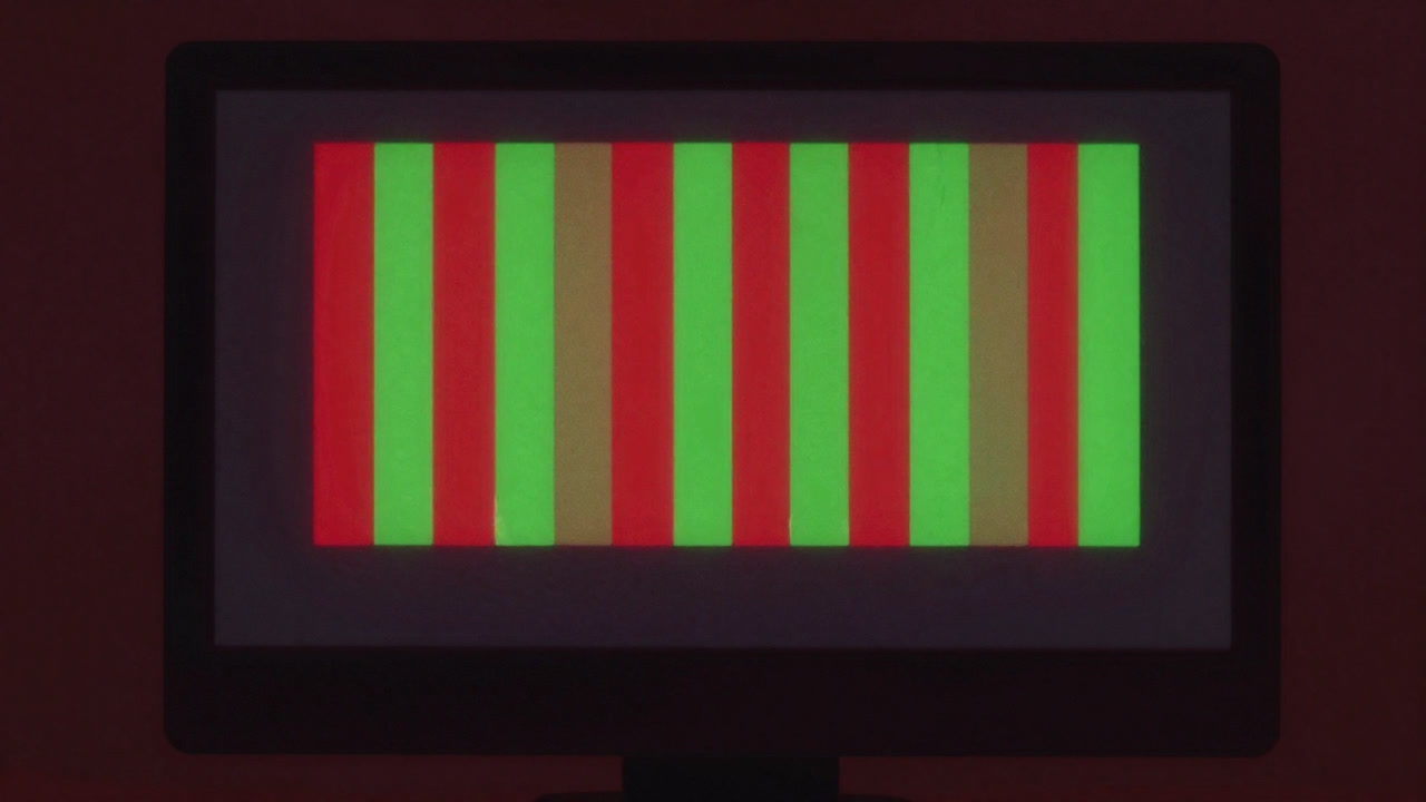 Close-up of a monitor glowing only with red and green test result bars in darkness