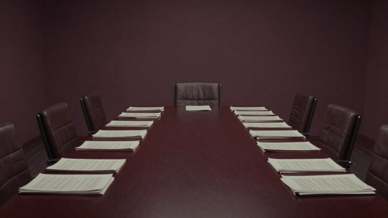 Photo of a conference room table piled high with reports and empty chairs