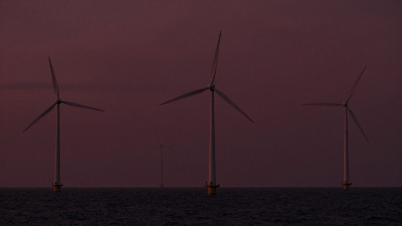 Photo of a row of wind turbines by the coast at dusk, exuding silent pressure.